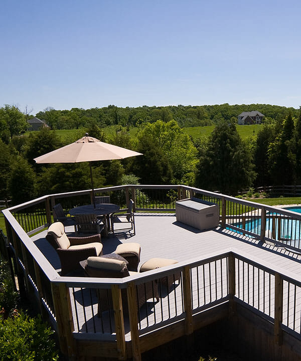 Modern wooden deck with seats and umbrella overlooking a blue pool